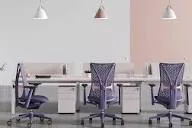 Sala de oficina moderna con tres puestos de trabajo, sillas ergonómicas de malla morada y escritorios blancos con lámparas colgantes