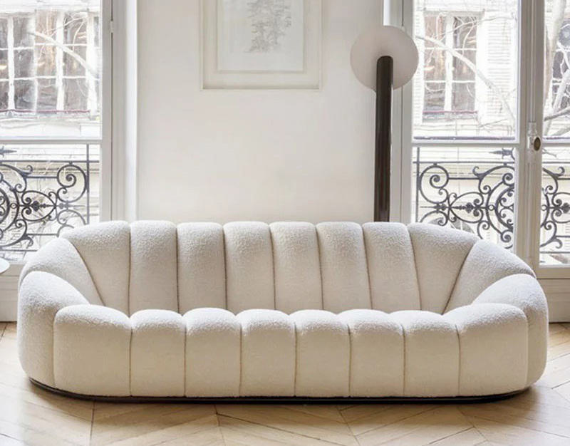 Salón pequeño con sofá de estructura de madera, alfombra clara y textiles neutros
