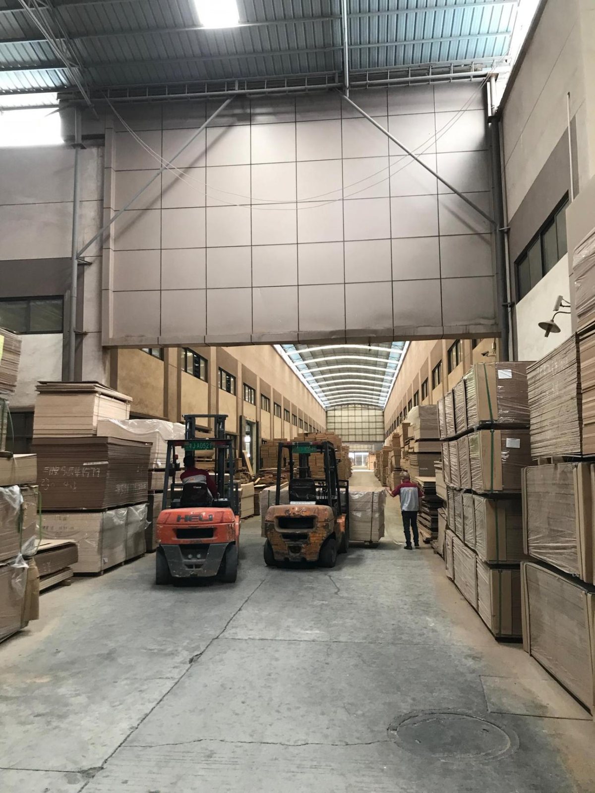 Almacén de tableros de la fábrica con carretillas elevadoras y materia prima de madera apilada en estanterías.