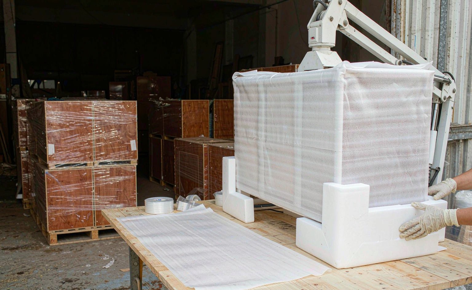 Armario envuelto en espuma de polietileno con esquineros blancos junto a cajas de madera contrachapada paletizadas en el almacén.