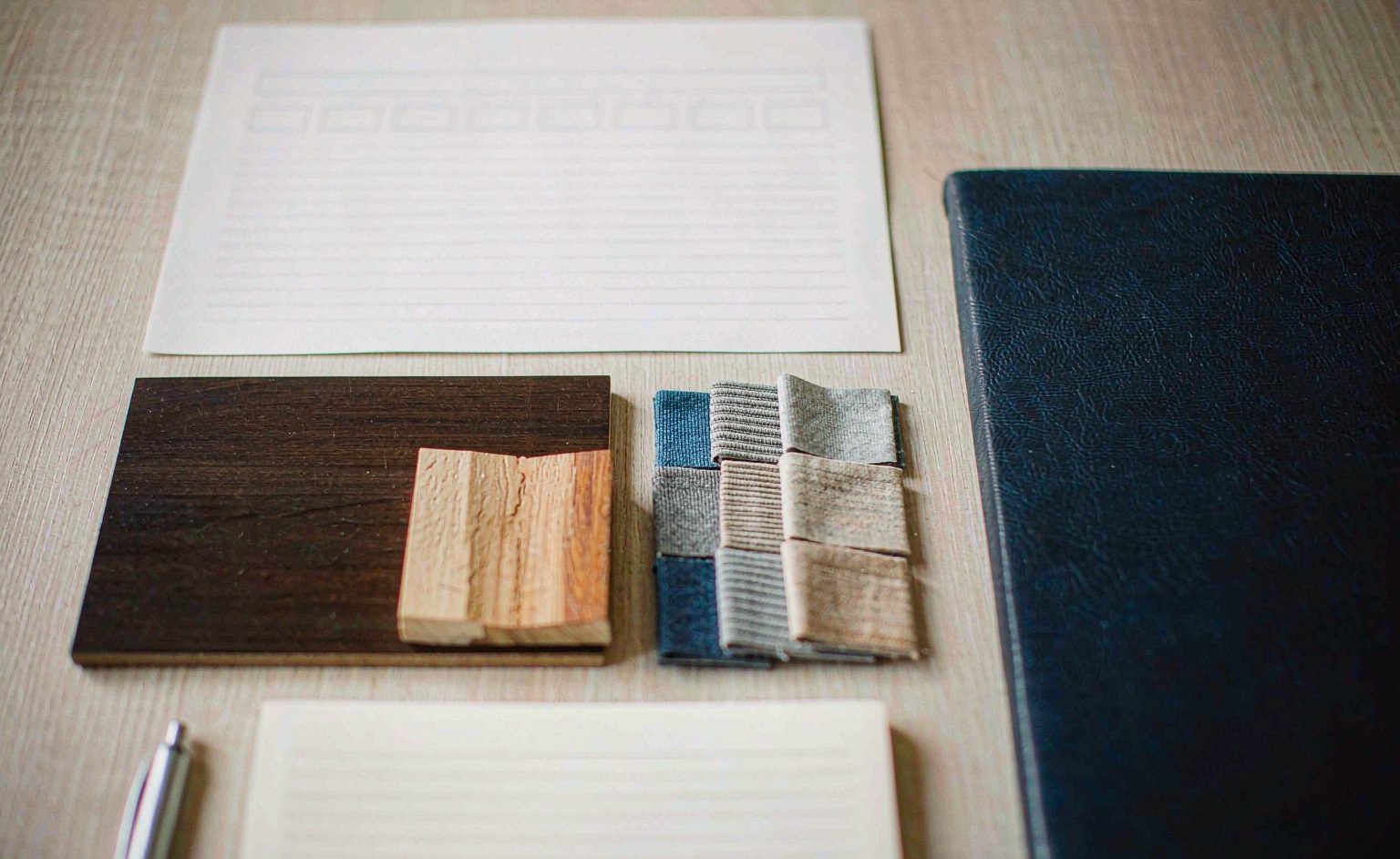 Muestras de chapas de madera y de tejido junto a documentos de la lista corta y una carpeta de itinerario sobre la mesa de preparación.