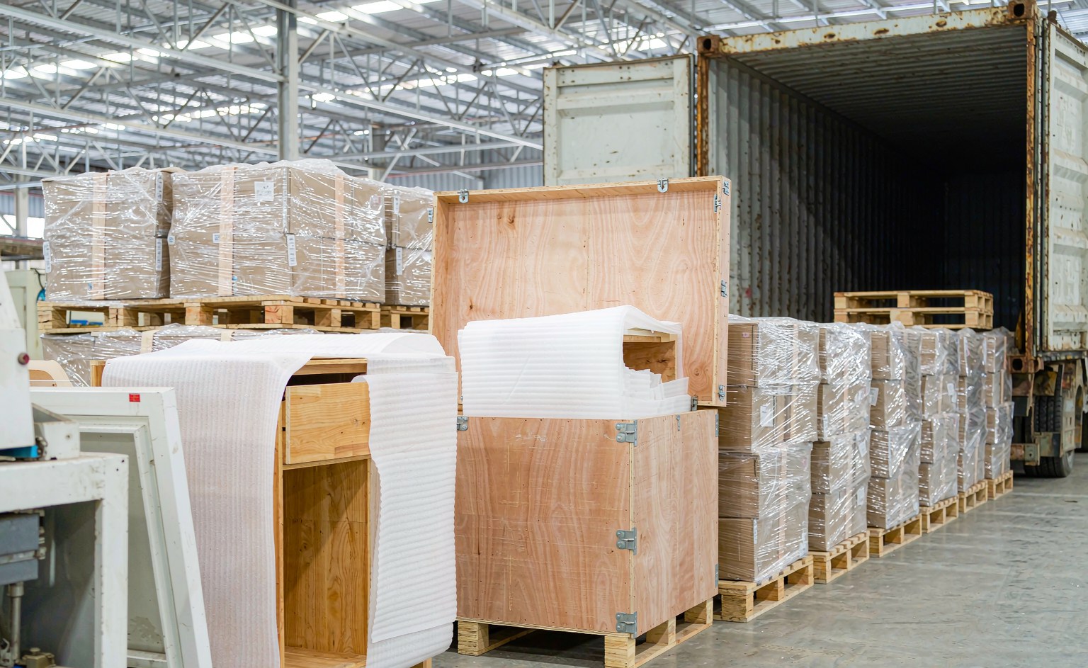 Cajas de madera contrachapada de exportación con esquineros y flejado sobre palé junto a un contenedor