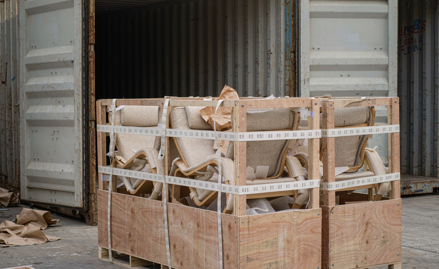 Cajas de madera contrachapada con esquineros y espuma EPE protegiendo brazos y patas de butacas, junto a un contenedor abierto en el patio de carga