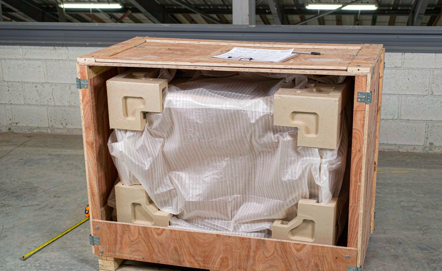 Caja de madera contrachapada abierta con esquineros y espuma EPE protegiendo la pieza de mobiliario en la zona de recepción