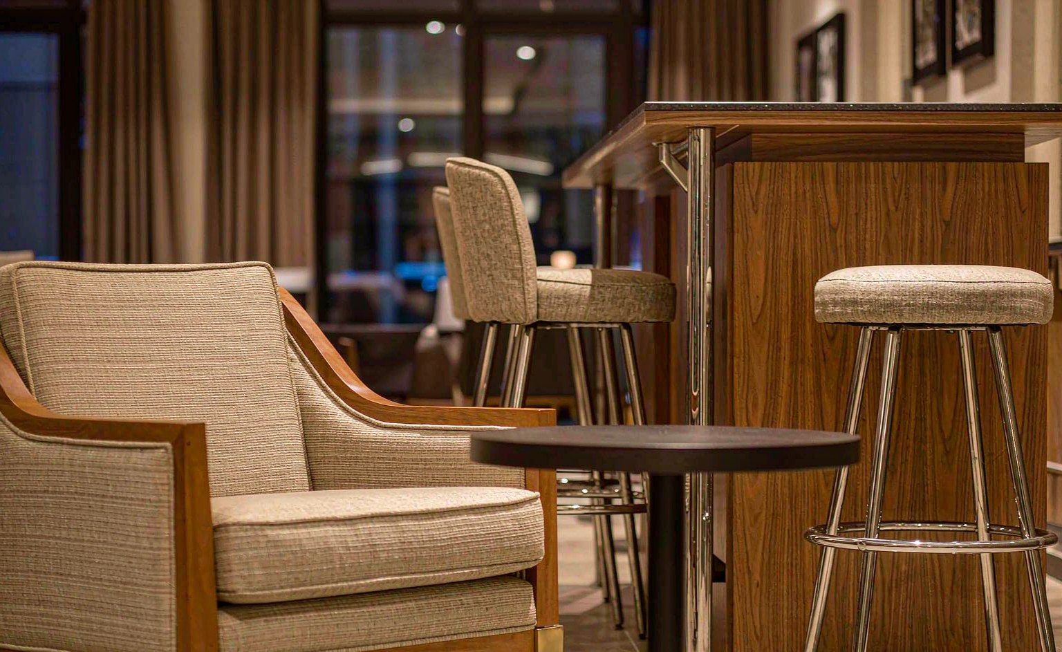Butaca tapizada de lounge de hotel junto a barra de madera con taburetes altos