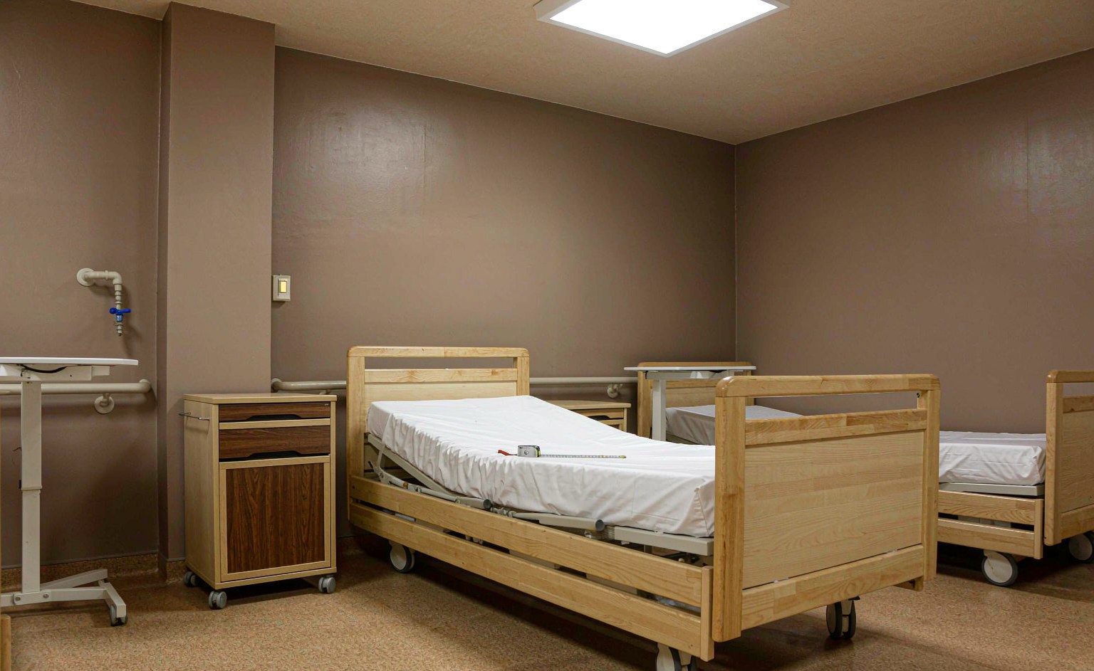 Cama articulada en posición baja y mesilla con ruedas bloqueables en la habitación muestra de una residencia