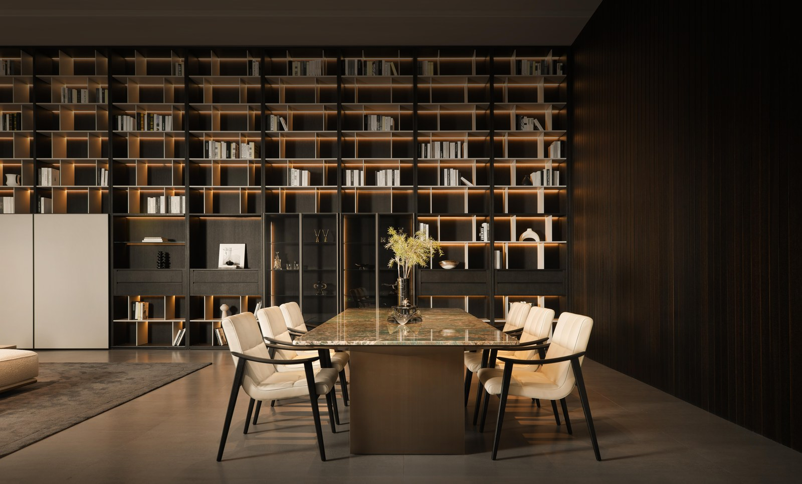 Zona de reunión de showroom de fábrica con mesa de piedra, sillería tapizada y pared de estanterías.